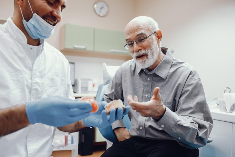 Foto de um dentista apresentando uma prótese dentária a um paciente idoso
